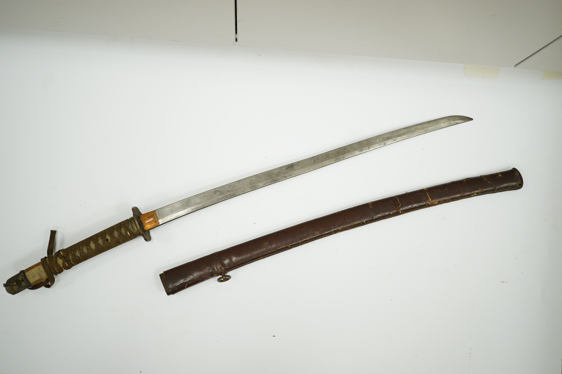 A WWII Japanese army officer’s Shingunto sword katana, blade 66.4cm, signed with Showa to stamp (tip of blade damaged), with unusual brass mounts, in its leather covered combat scabbard. Condition - poor to fair